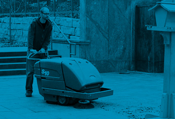 worker using outdoor Tennant floor sweeper to clean facilities