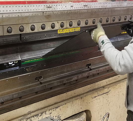 Tennant Production staff member forming metal part with press brake Tennant Production staff member forming metal part with press brake