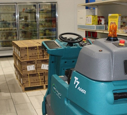 Tennant's T7AMR robotic floor cleaning machine using artificial intelligence and smart sensors to navigate around a pallet of food in a grocery store. Tennant's T7AMR robotic floor cleaning machine using artificial intelligence and smart sensors to navigate around a pallet of food in a grocery store.
