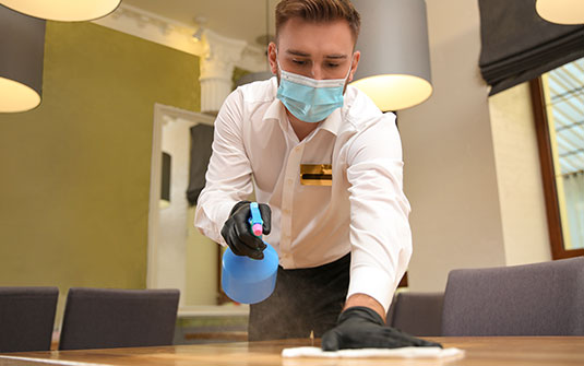 custodian staff cleaning surface of table with face mask, gloves and googles on. custodian staff cleaning surface of table with face mask, gloves and googles on.