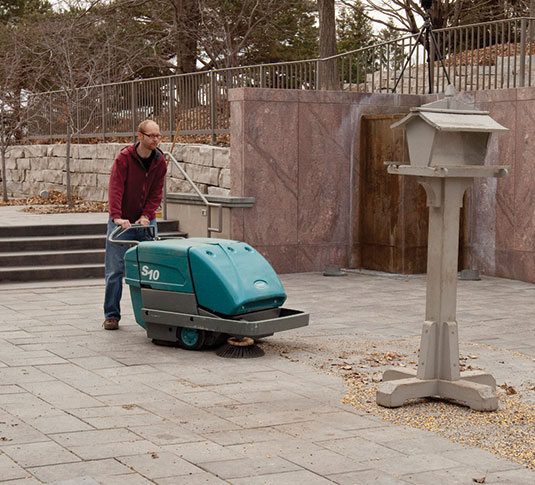 S10 Walk-Behind Sweeper picks up debris on a sidewalk before it can be tracked into a building.