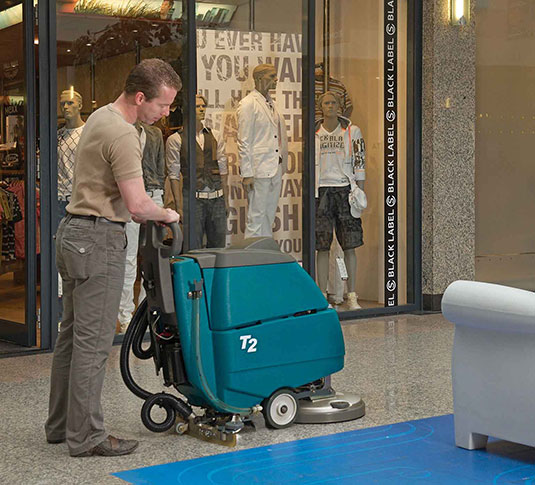une équipe de nettoyage utilisant la récureuse à plancher à commande arrière de Tennant dans la zone principale du magasin de détail une équipe de nettoyage utilisant la récureuse à plancher à commande arrière de Tennant dans la zone principale du magasin de détail