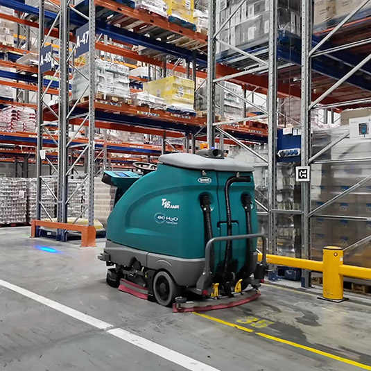 Een Tennant automatische schrobzuigmachine die een magazijn reinigt.